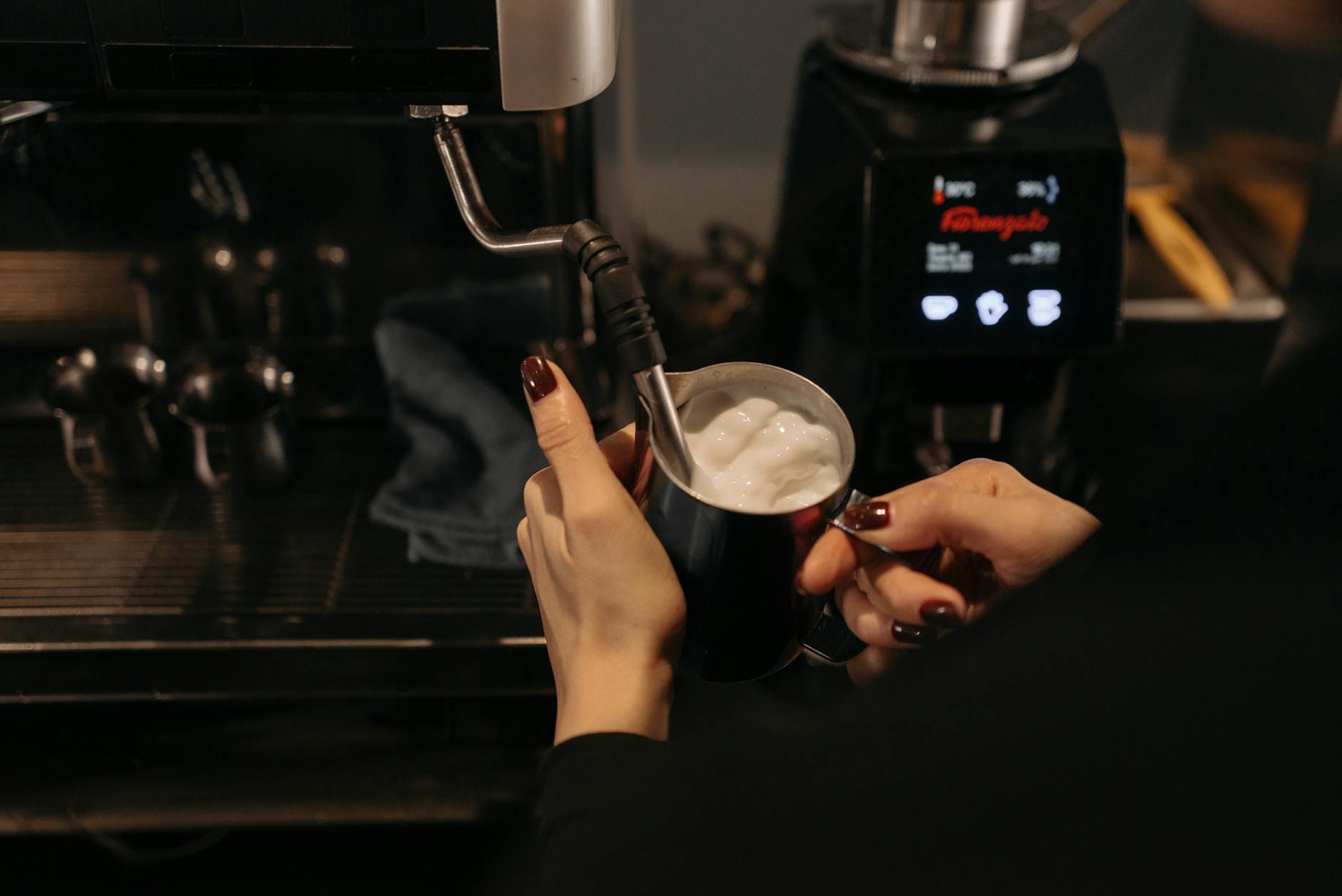 Barista spienia mleko dyszą pary podczas przygotowywania cappuccino
