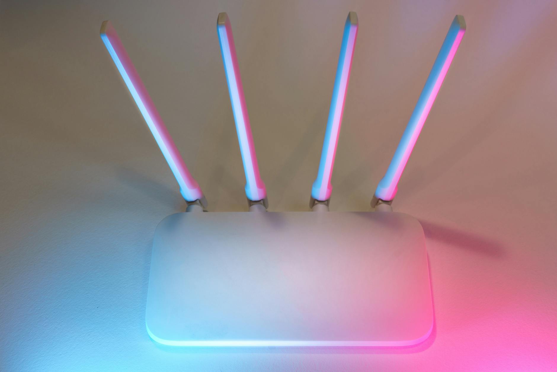 Domowe Wi‑Fi naprawdę bezpieczne: praktyczny przewodnik krok po kroku Nowoczesny biały router Wi‑Fi z czterema antenami w niebiesko-różowym świetle